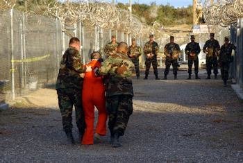 US Army Military Police escort a detainee to his cell in Camp X-Ray at Naval Base Guantanamo Bay, Cuba in 2002.