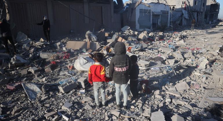Three children stand amidst the rubble of their destroyed home in Rafah.