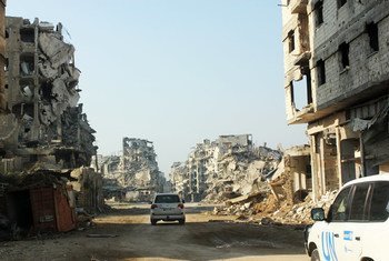 UN vehicles travel along a road lined with remnants of destroyed buildings, Homs, Syria. (file)
