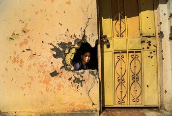 A young girl looks through a hole in the wall from damage from conflict in a school in Ramadi, Anbar Governorate, Iraq.